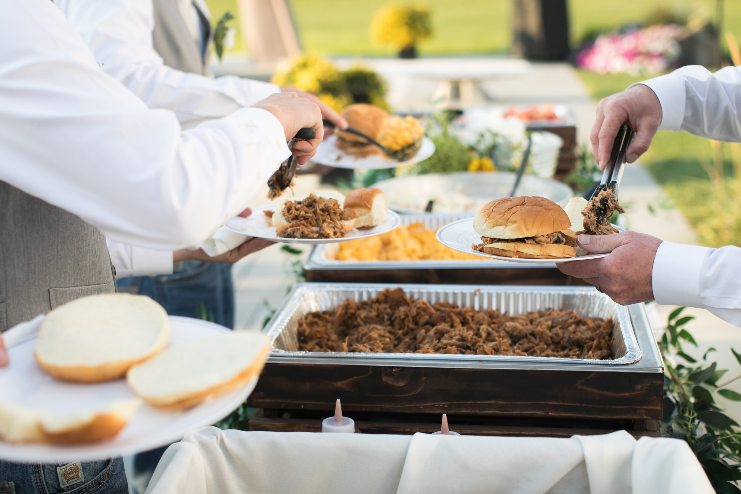 People serving sandwiches and pulled pork at an outdoor buffet table