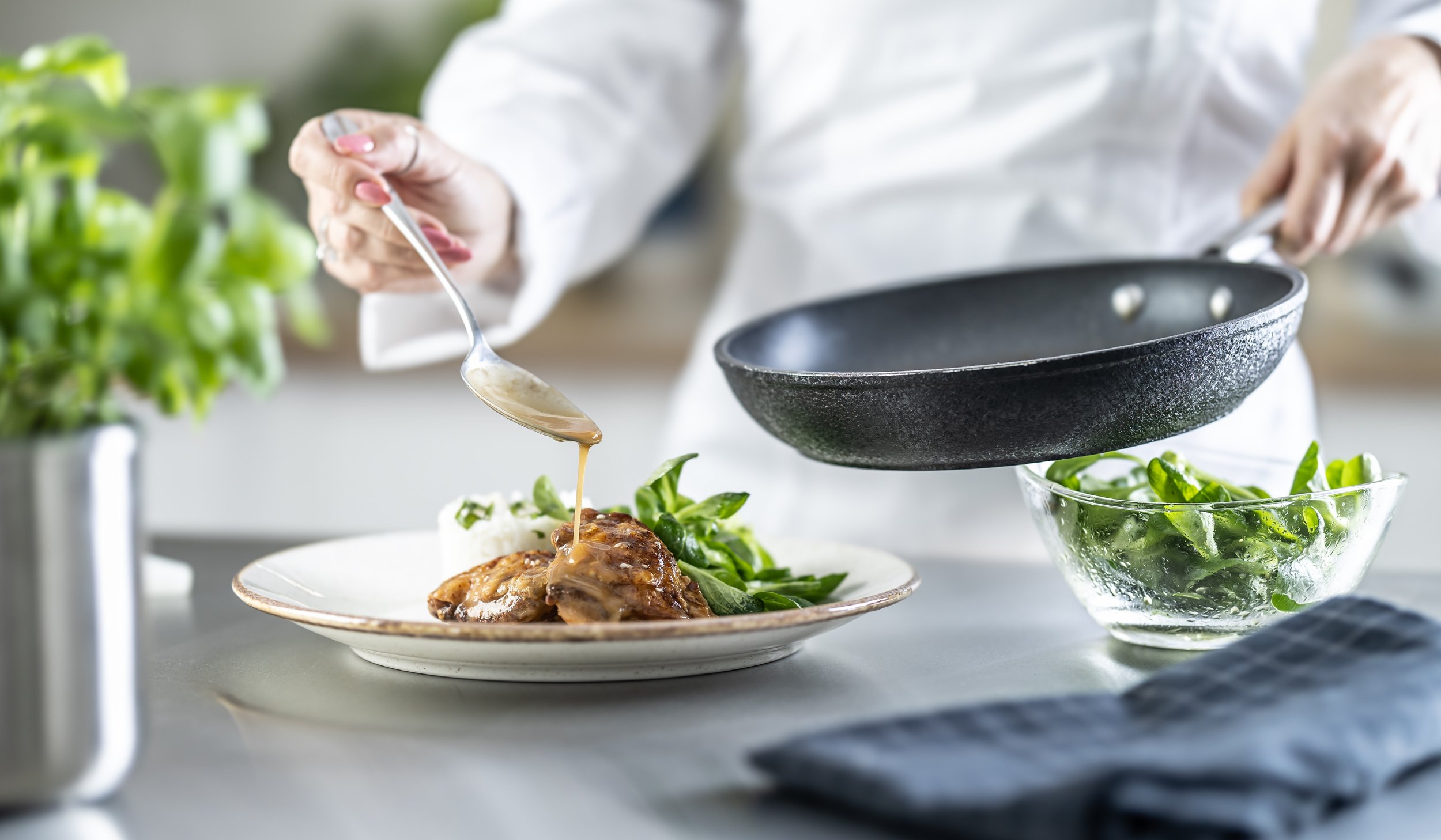 Person pouring sauce onto a plate of cooked chicken and greens