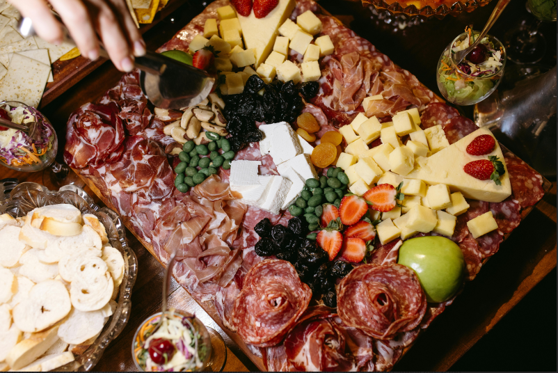 Charcuterie board with cheeses, cured meats, strawberries, blueberries, green olives, and crackers.